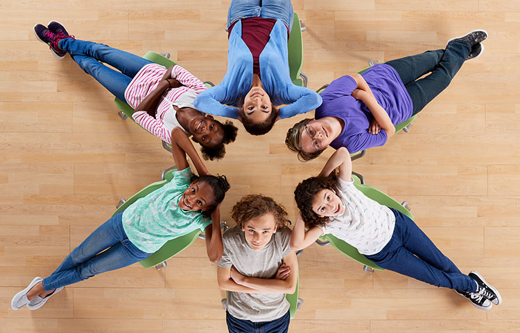 An overhead photograph of 6 school kids relaxing on classroom chairs