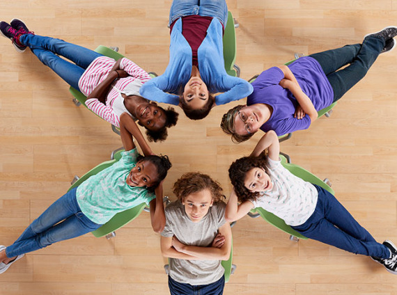 An overhead photograph of 6 school kids relaxing on classroom chairs