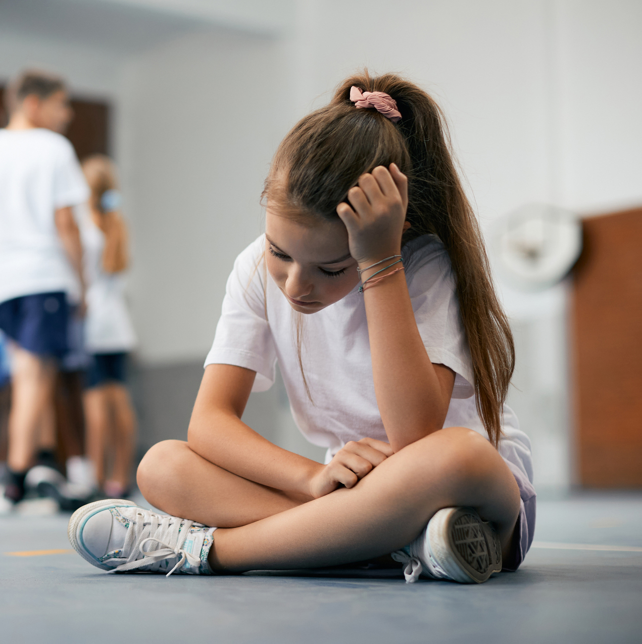 A photograph of a Sad schoolgirl feeling left out during physical activity class at school gym.